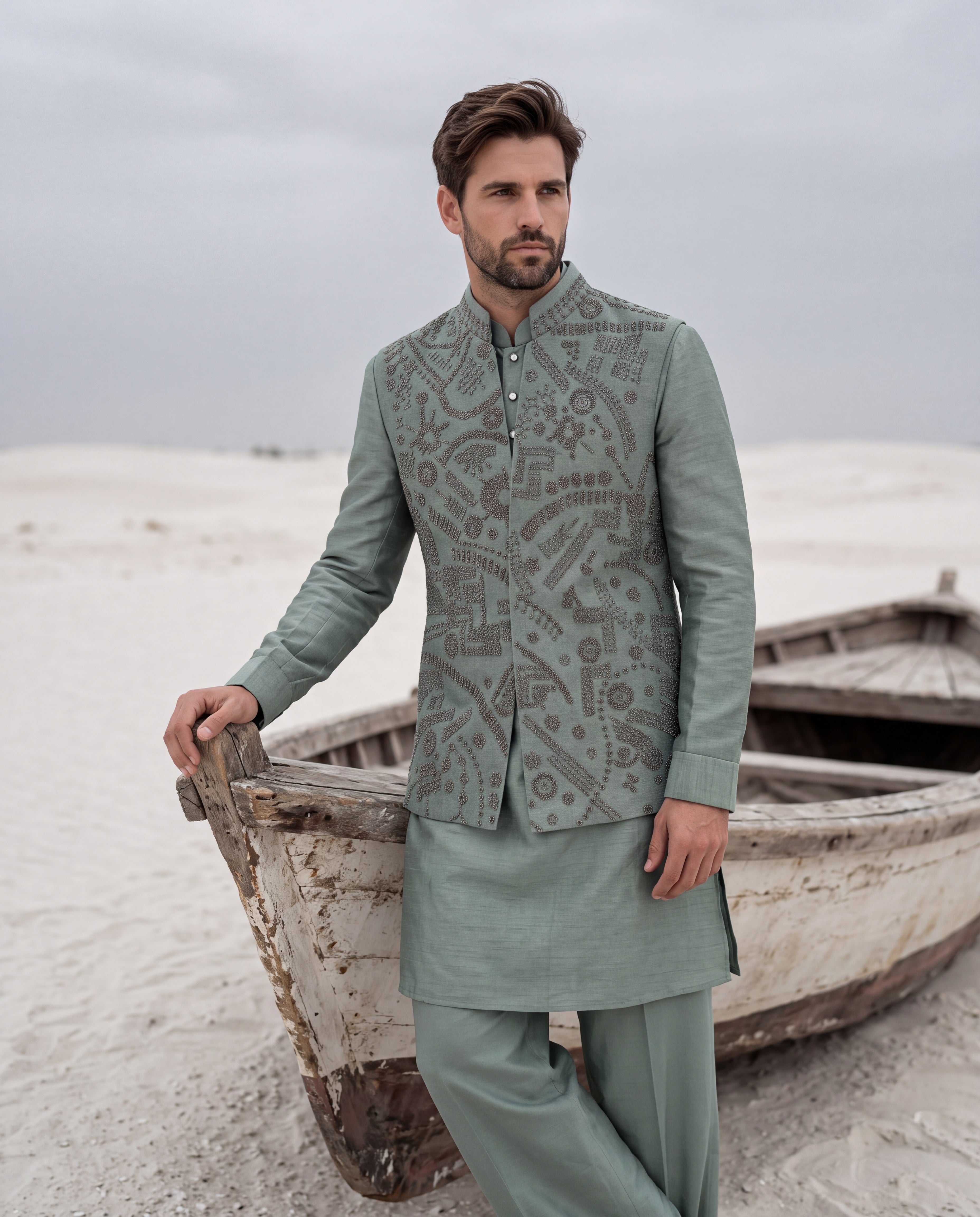 Teal green textured velvet waistcoat with metallic hand embroidery detailing, paired with a silk kurta and matching aligadhi pants.