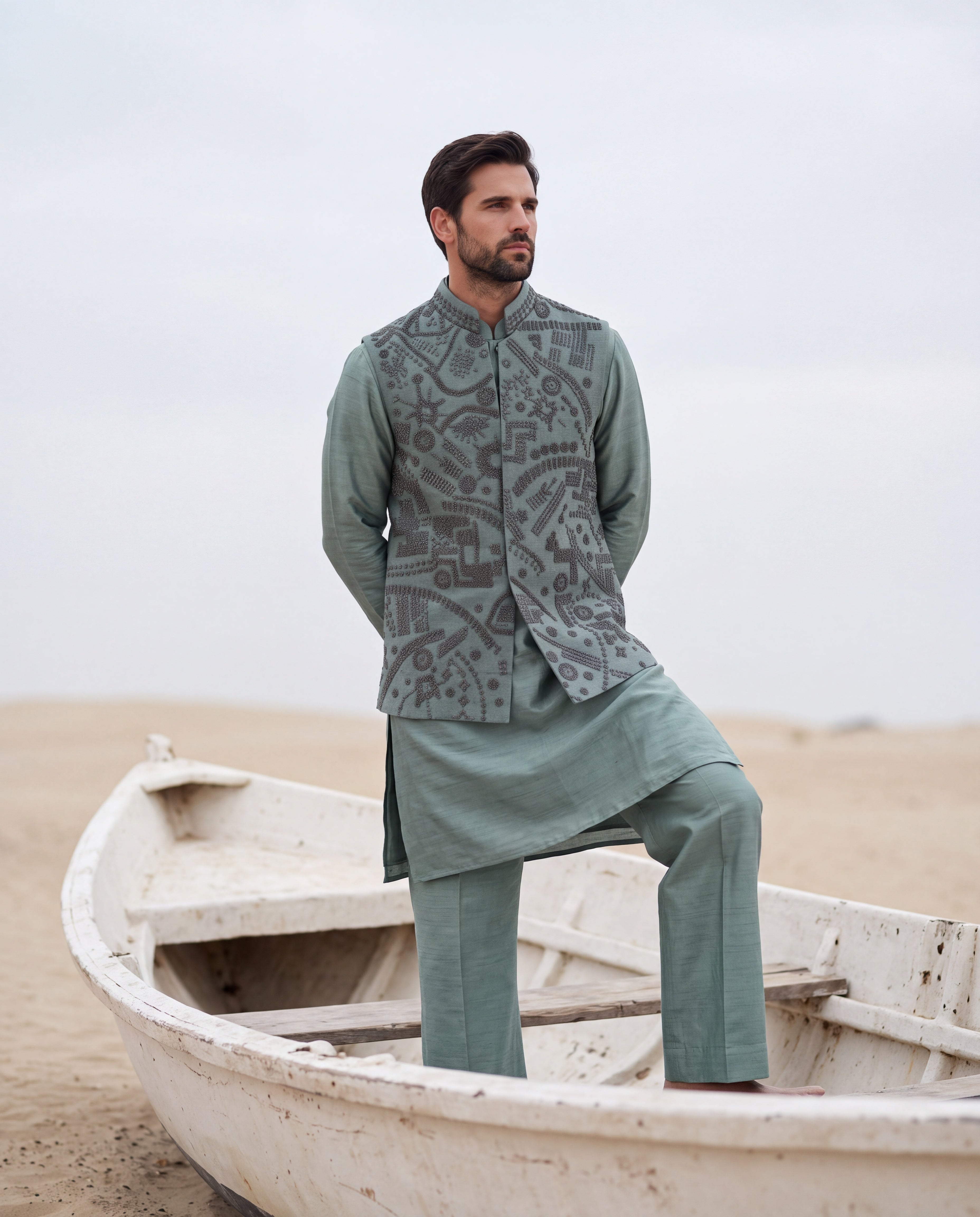 Teal green textured velvet waistcoat with metallic hand embroidery detailing, paired with a silk kurta and matching aligadhi pants.