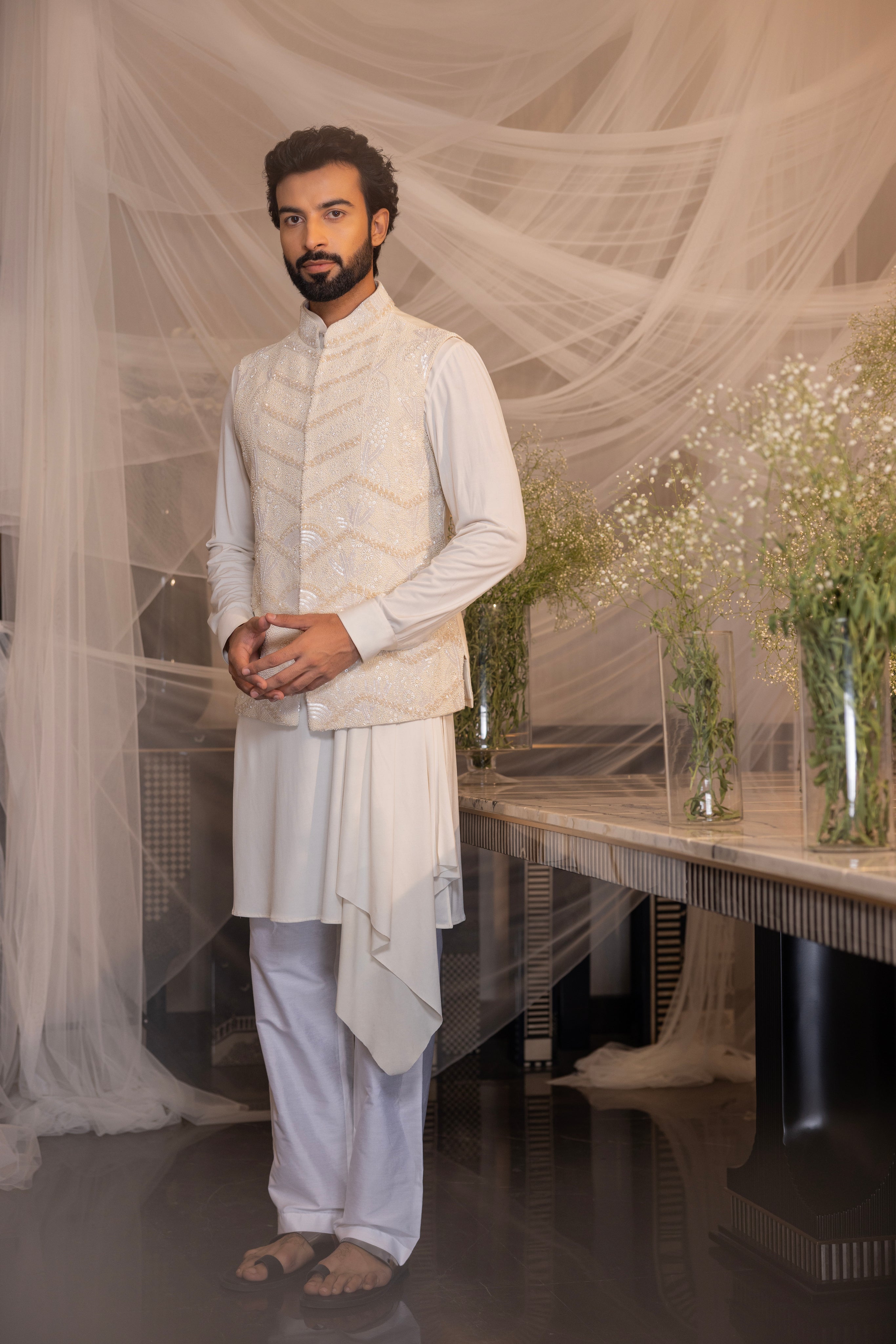Ivory waistcoat with intricate montone hand-embroidery paired with a draped kurta and matching aligadhi.