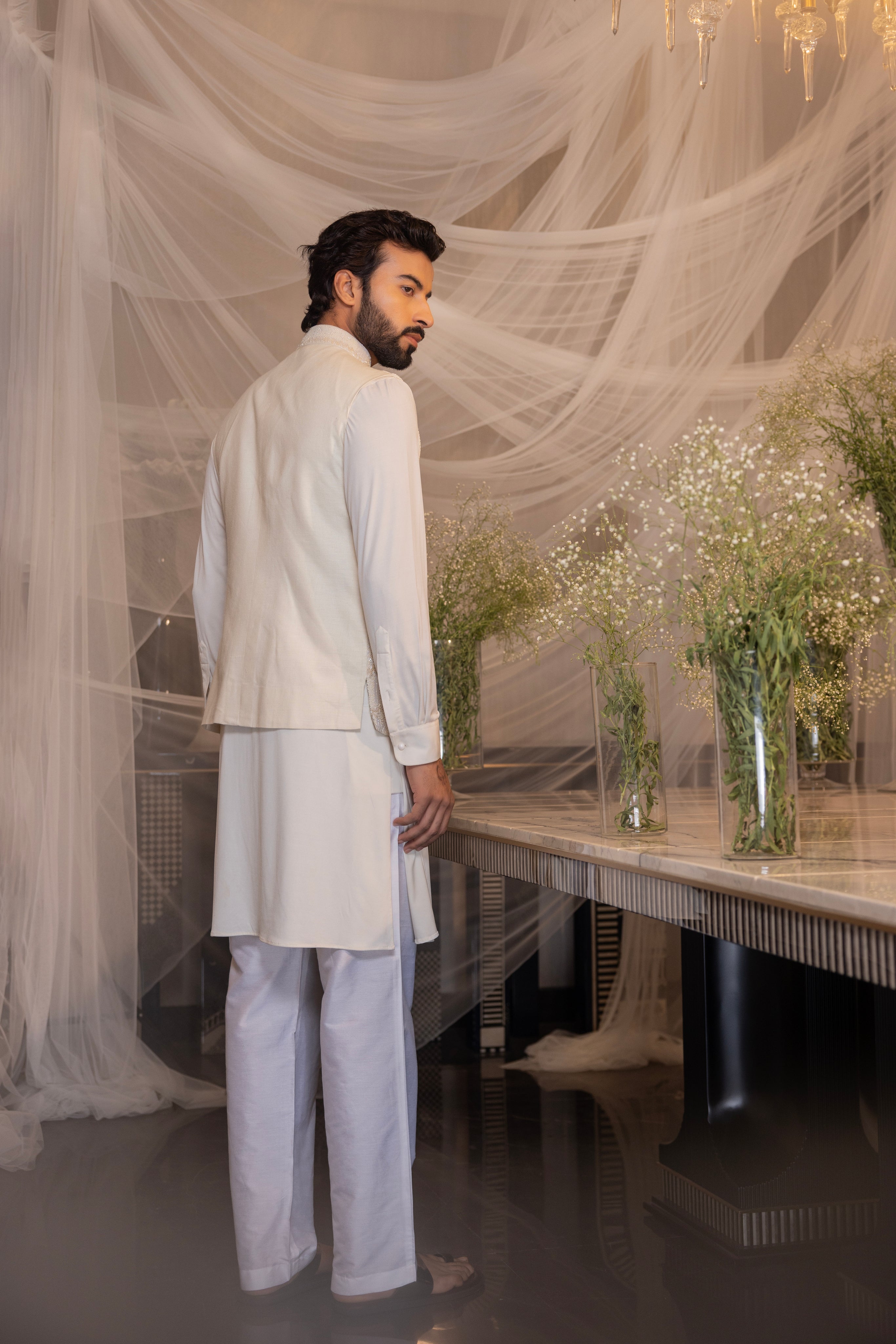 Ivory waistcoat with intricate montone hand-embroidery paired with a draped kurta and matching aligadhi.