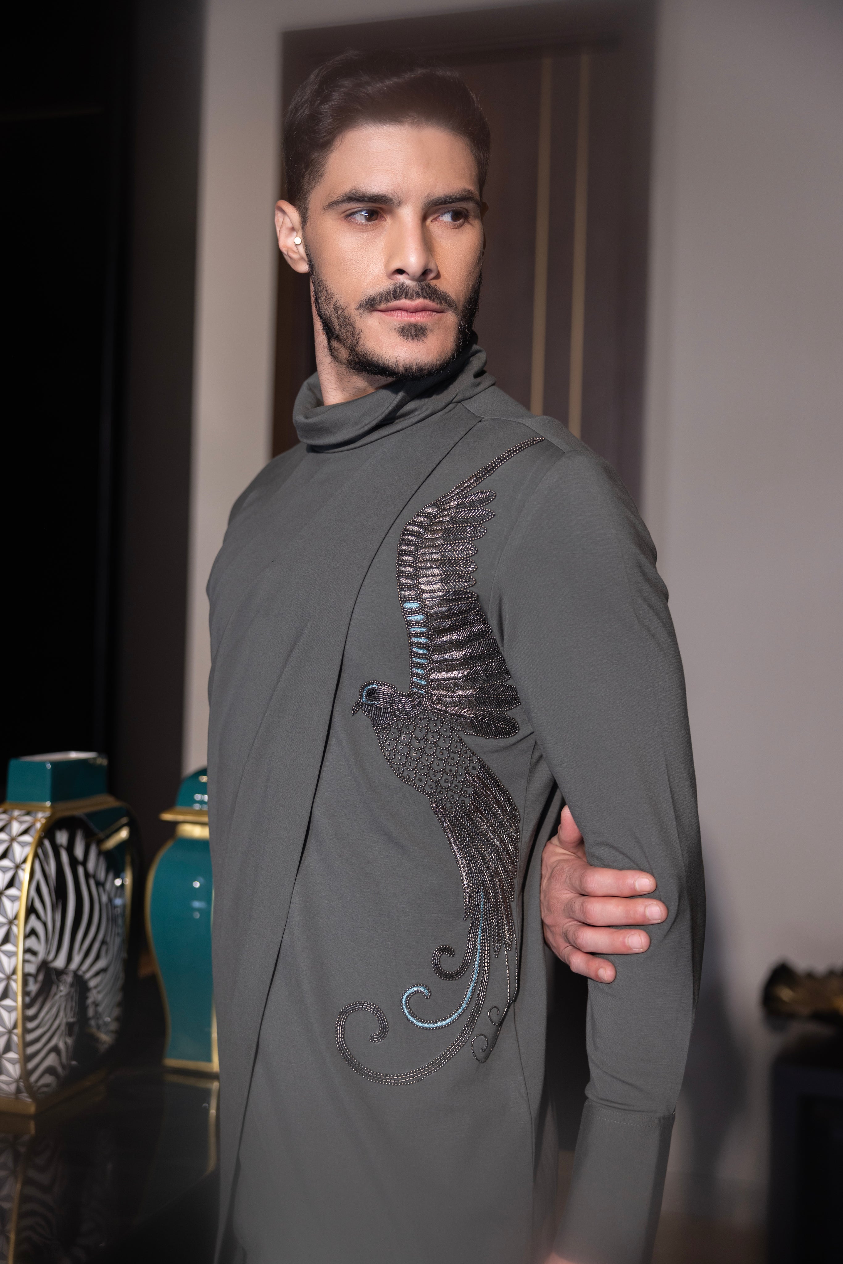 Olive green asymmetrical kurta with hand-embroidered bird motif  paired with a matching aligadhi set.