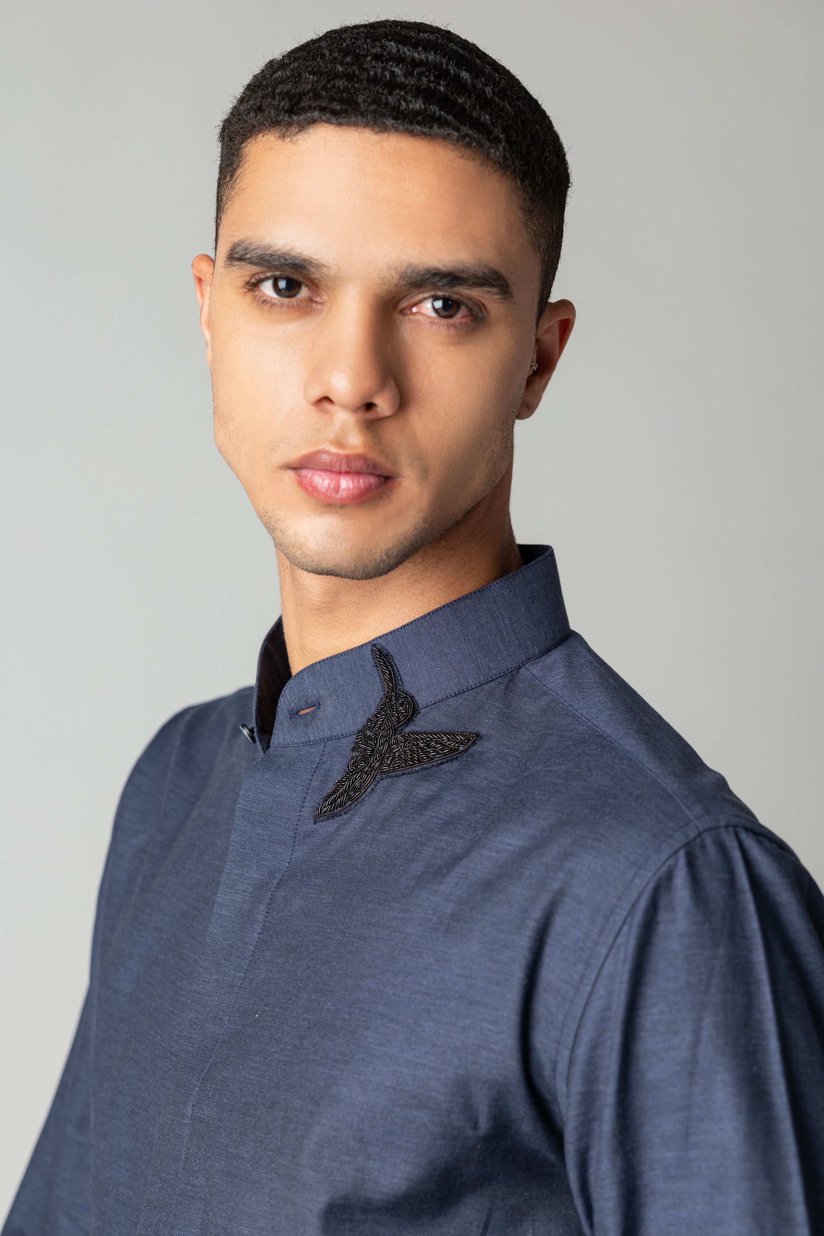 Blue knit shirt with hand-embroidered bird motif on Mandarin collar